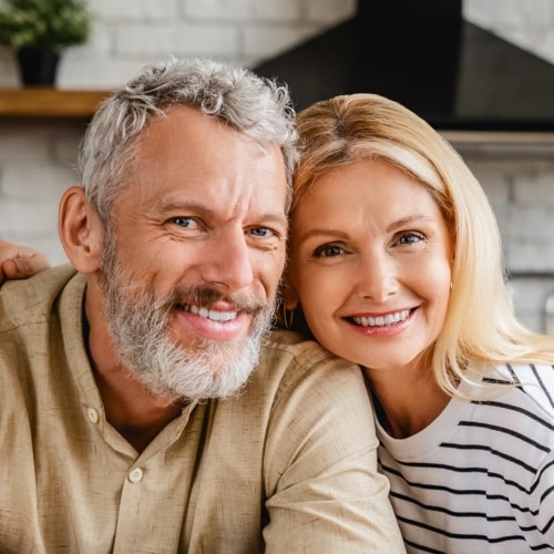 Pareja de mediana edad sonriendo sentada junta en una cocina luminosa mirando a la camara